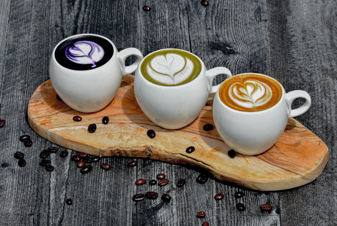 Three lattes with latte art on a wooden serving board